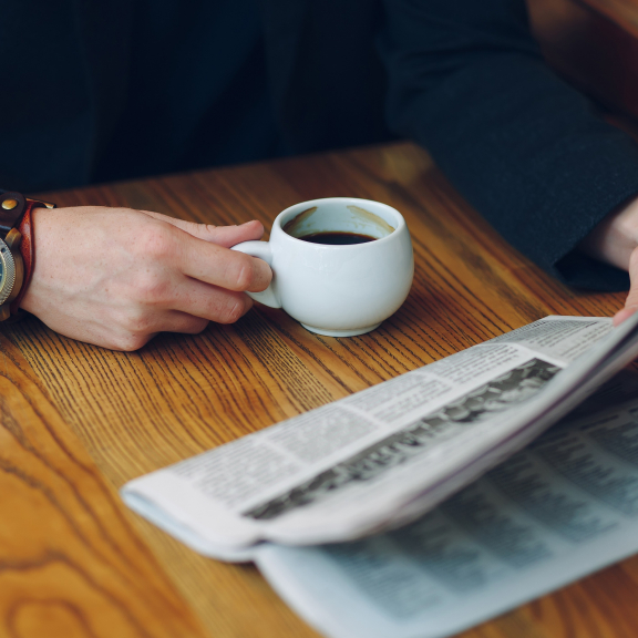 Person liest Zeitung und trinkt Kaffee – Moment der Information und Reflexion über das aktuelle Tagesgeschehen.