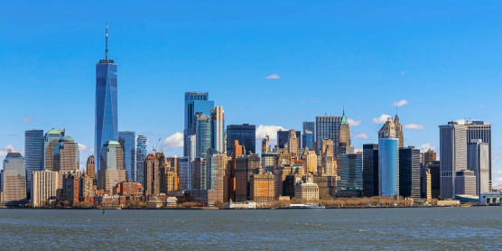 Auswandern nach USA – Freiheitsstatue vor Skyline von New York City bei blauem Himmel