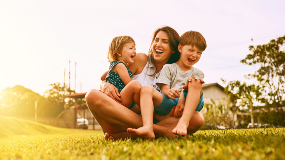 Glückliche Mutter spielt mit ihren Kindern im Garten – ideal für Tipps zu Umzug mit Kindern