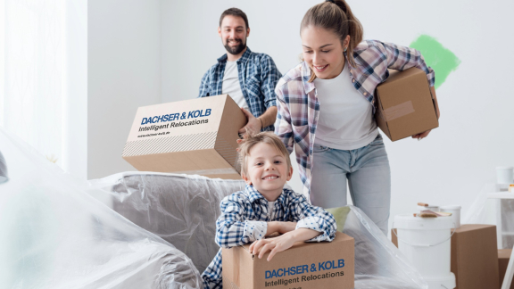 Familie beim Umzug mit Kindern, lachend und Kartons tragend in neuem Zuhause