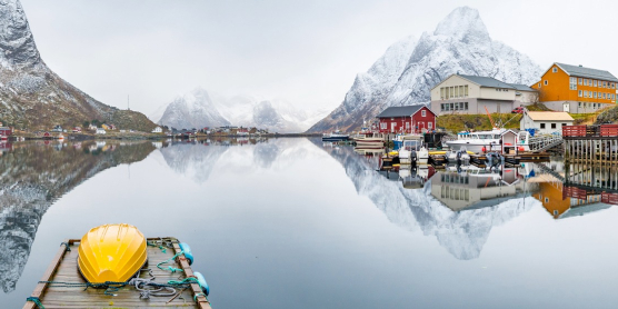 Fjorddorf in Norwegen mit schneebedeckten Bergen und Spiegelung im ruhigen Wasser