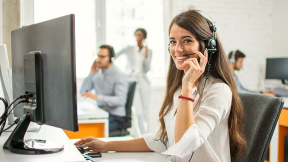 Eine lächelnde Mitarbeiterin im Kundenservice von DACHSER & KOLB berät Kunden per Headset am PC über den internationalen Luftfracht-Umzug.