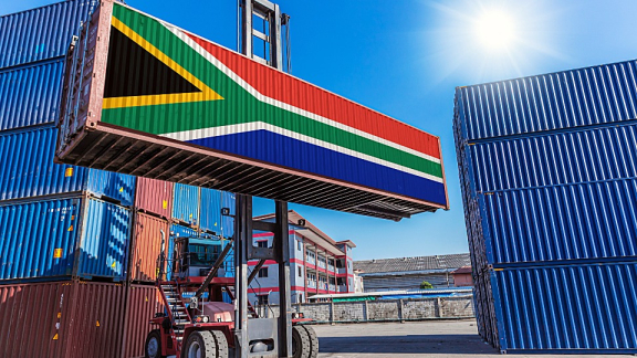 Ein Containerstapler verlädt einen Übersee-Container mit südafrikanischer Flagge im Hafen für den Container-Umzug nach Südafrika mit DACHSER & KOLB.