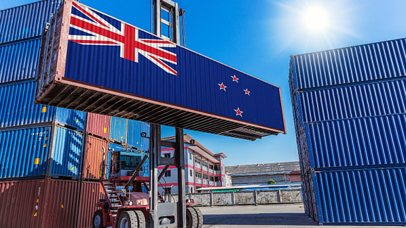 Ein Containerstapler verlädt einen Übersee-Container mit neuseeländischer Flagge für den Container-Umzug nach Neuseeland mit DACHSER & KOLB.