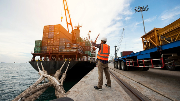 Hafenmitarbeiter überwacht die Verladung von Frachtcontainern auf ein Containerschiff für den Überseeumzug mit DACHSER & KOLB.